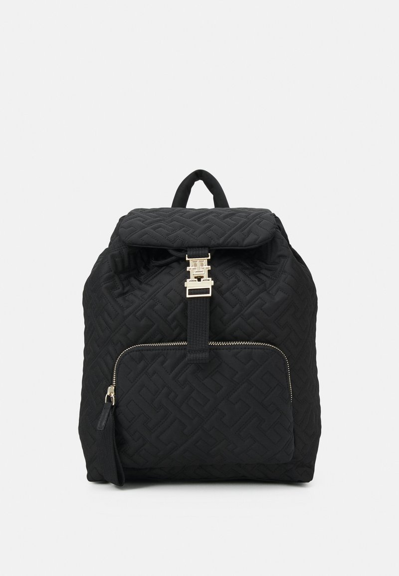 Black quilted backpack with geometric pattern, gold hardware, top flap, and front zip pocket. Fabric texture appears soft and durable.