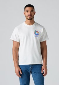 Witte katoenen t-shirt met korte mouwen, voorzien van een kleurrijke grafische afbeelding op de linkerborst die bergen en de tekst "Levi's" toont.