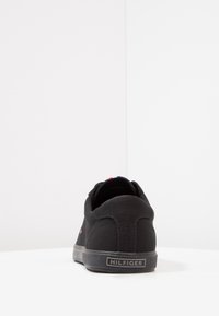 Schwarze Canvas-Sneaker mit glatter Textur, ausgestattet mit einer gepolsterten Ferse, Gummisohle und einem kleinen Logo-Tag an der Seite.