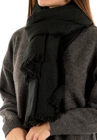 Sciarpa verde scuro realizzata in morbido tessuto a trama, con motivo a spina di pesce e estremità frangiate, indossata sopra un maglione grigio.