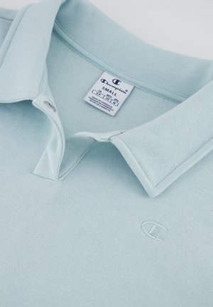 Hellblaues Poloshirt mit weicher Textur, ausgestattet mit einem Knopfkragen und einem kleinen gestickten Logo auf der Brust. Das Etikett zeigt die Größe klein an.