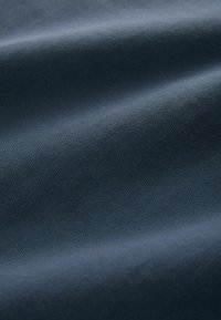 Textiles mit Struktur in Dunkelblau, die ein feines geripptes Muster zeigen, wobei sanfte, glatte Oberflächenfalten Tiefe und Dimension erzeugen.