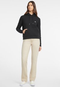Felpa nera con tasca a marsupio, cappuccio regolabile con cordini e un piccolo logo sul petto, abbinata a jeans dritti color beige chiaro.