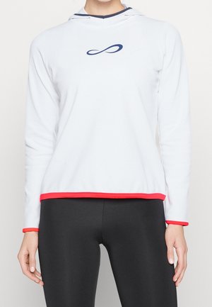 Person trägt einen weißen Kapuzenpullover mit langen Ärmeln, blauem Unendlichkeitssymbol, rotem Rand und schwarzen Leggings, dargestellt von Hals bis Hüfte.