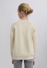 Sweat-shirt couleur crème avec encolure ronde, poignets côtelés et coupe décontractée. Texture lisse avec manches montées et ourlet droit.