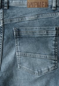 Los jeans de mezclilla de color azul claro cuentan con un bolsillo trasero estándar y una etiqueta de cuero con "ONEMEN" grabada en ella. La tela tiene una textura suave.
