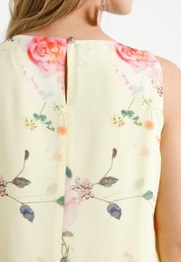 Letní šaty bez rukávů s květinovým vzorem v pastelově žluté barvě, s detailem malého výřezu na zádech a lehkou, vzdušnou látkou s akvarelovými květinovými tisky.