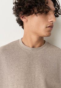 Lichtbeige crewneck-trui met een getextureerde stof. Heeft een relaxte pasvorm en een zachte, gladde oppervlak. Minimalistisch ontwerp zonder zichtbare logo's.