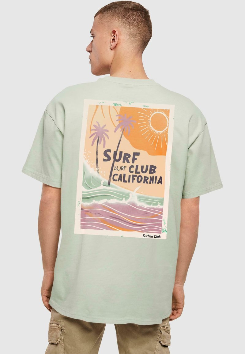 Tricou din bumbac verde deschis, cu un design grafic retro pe spate, reprezentând palmieri, valuri și textul "Surf Club California."