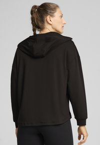 Sudadera negra con capucha, de mangas largas, corte relajado y textura suave. Presenta una gran capucha y aberturas en los laterales del dobladillo.