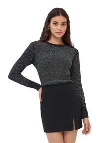 Maglione nero a maniche lunghe con un motivo di lavorazione a maglia testurizzato, abbinato a una gonna nera aderente mini con uno spacco laterale.