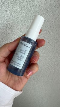 Blauwe doorzichtige sprayfles met witte dop, gelabeld "KERASTASE," met volumizing spray. 150 mL/5,1 fl oz. Soepele textuur.
