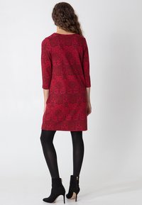 Czerwona sukienka z rękawami do połowy przedramienia, kwiatowym wzorem i luźnym krojem. Noszona z czarnymi, kryjącymi rajstopami oraz botkami za kostkę z zamkiem błyskawicznym.
