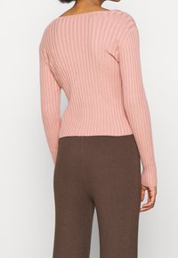 Różowy prążkowany sweter z długimi rękawami i szerokim dekoltem, zestawiony z brązowymi prążkowanymi spodniami. Materiał wygląda na miękki i fakturowany.