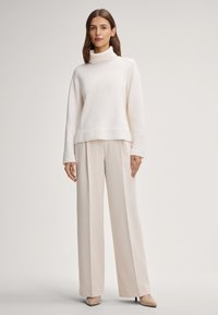 Cremfarbener Rollkragenpullover mit geripptem Saum und Bündchen, kombiniert mit hellbeigen weit geschnittenen Hosen. Glatter Stoff, entspannte Silhouette, minimalistisches Design.
