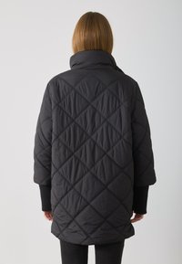 Schwarze, gesteppte Parka mit hohem Kragen, Oversized-Design und Rautenmustern. Die Ärmelbündchen sind gestrickt, was den strukturierten Look verstärkt.