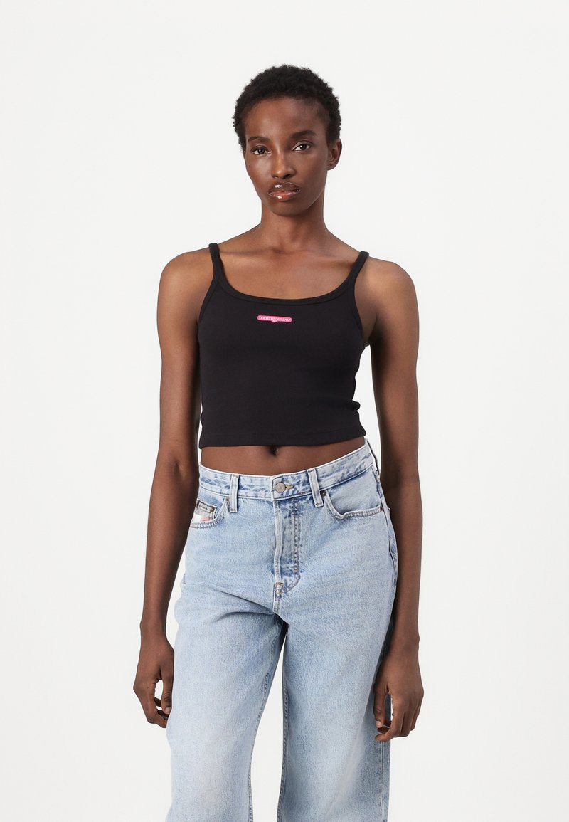 Top corto nero con spalline sottili, con un logo rosa al centro. Abbinato a jeans di denim azzurro chiaro a vita alta.