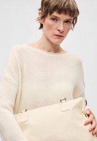 Beżowa skórzana torebka o gładkiej fakturze i srebrnych elementach metalowych. Torebka posiada dwa górne uchwyty i elegancki, minimalistyczny design.