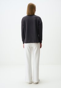 Felpa grigia oversize con spalle scese, maniche lunghe e una texture liscia, abbinata a pantaloni bianchi a gamba larga e sneakers.