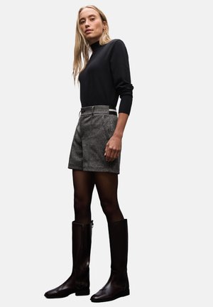 Un pull à col roulé noir, un short gris texturé avec poches, des bottes marron jusqu'aux genoux avec zippers, un design minimaliste, une silhouette ajustée.