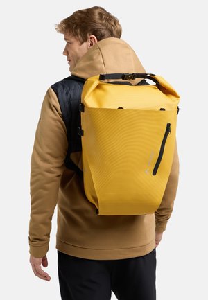 Sac à dos imperméable jaune avec une surface texturée, des bretelles ajustables et une poche zippée latérale, porté sur le dos d'une personne.