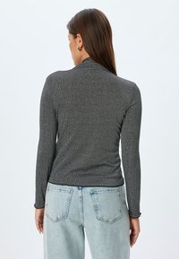 Graues, geripptes Langarmshirt mit schmaler Silhouette und rundem Ausschnitt, das eine feine Textur und gewellte Kanten an den Ärmeln aufweist, kombiniert mit hellen Jeans.