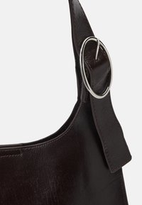 Dark brown leather handbag with a smooth texture and a round silver hardware accent on the strap. Features a soft, curved shape.