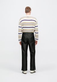 Prugasta majica dugih rukava u krem, ljubičastoj i bež boji, uparena sa sjajnim crnim trapericama. Pogled s leđa, s vidljivim tenisicama.