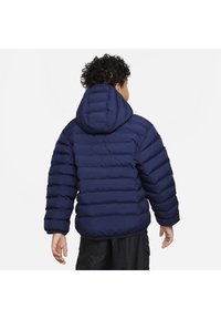 Giacca puffer blu navy con design trapuntato, cappuccio e polsini elasticizzati. Presenta una texture liscia e una vestibilità comoda, vista da dietro.
