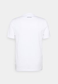 Valkoinen puuvillapaita, jossa on pyöreä pääntie ja lyhyet hihat. Takana on pieni painettu "CALVIN KLEIN" -logo lähellä kaula-aukkoa.