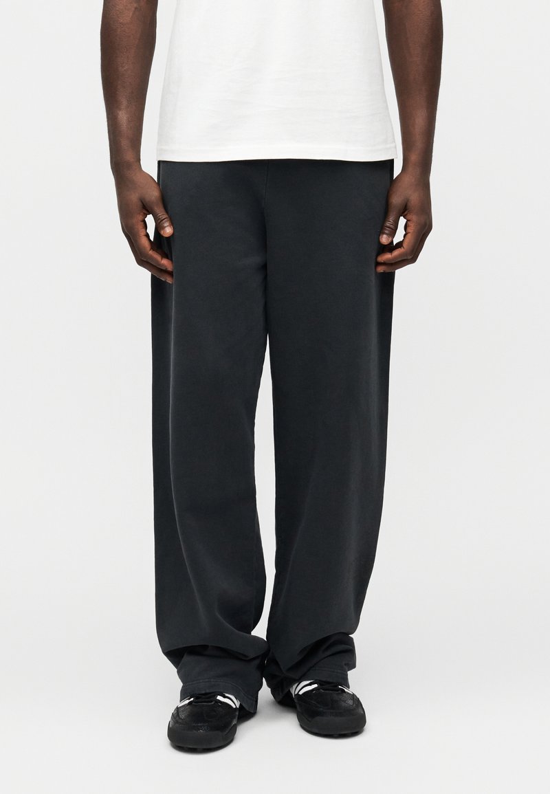 Fekete, széles szárú melegítőnadrág puha pamutkeverékből, bő szabással és bordás mandzsettákkal, fekete, fehér díszítésekkel ellátott sportcipővel párosítva.