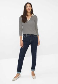 Polo a maniche lunghe a righe con colletto beige, abbinato a jeans di denim blu scuro, con maniche arrotolate e scarpe flat chiare.