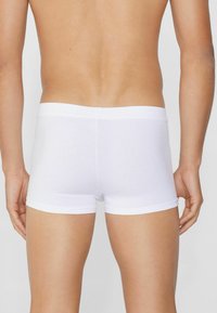 Białe bokserki wykonane z miękkiego, elastycznego materiału. Posiadają gładki fason, elastyczny pas i długość do połowy uda. Gładka faktura.