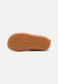 Semelle d'une chaussure en matériau en caoutchouc, de couleur orange, avec des motifs circulaires et des rainures texturées pour l'adhérence. Nom de la marque « CAMPER » embossé sur le côté.