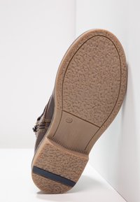 Sole hnědé boty s texturovanou gumovou podrážkou a viditelnou velikostí 37, umístěná proti bílé rohové zdi.