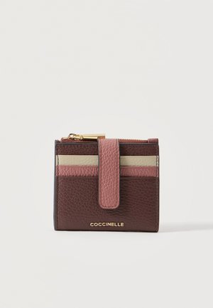 Portefeuille compact en cuir tricolore avec des emplacements pour cartes, une sangle à fermeture pression, un compartiment zippé et le logo "Coccinelle" doré en bas.
