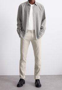 Camicia a quadretti nera e bianca, pantaloni beige e scarpe nere. Tessuto liscio con una vestibilità su misura e design a gamba dritta.
