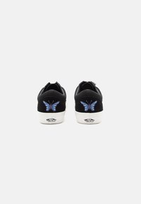 Black suede sneakers with a white sole, featuring blue butterfly embroidery on the heel and "Vans Off the Wall" logo.