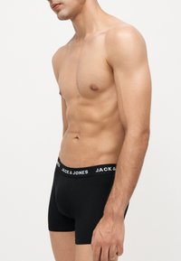 Mannequin masculin en forme portant un boxer noir de la marque Jack & Jones, debout devant un fond blanc uni.
