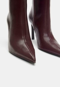 Botine de piele burgundy, cu vârf ascuțit, tocuri înalte stiletto, închidere laterală cu fermoar și textură netedă, lustruită.