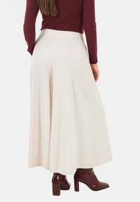 Gonna lunga color crema plissettata con una cintura strutturata, abbinata a stivali marroni con tacco fino al ginocchio. Texture liscia e silhouette ampia.