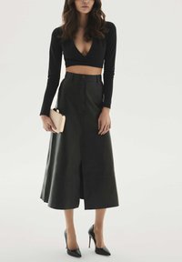 Juoda ilgomis rankovėmis trumpa palaidinė su gilia V formos iškirpte, derinama su aukštakulne odine sijonu. Modelis laiko mažą smėlio spalvos delninę ir dėvi juodus aukštakulnius.