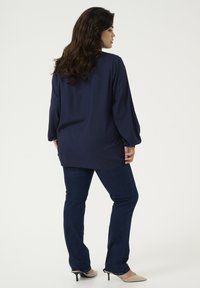 Laivastonsininen pitkähihainen paita, jossa on kuvioitu pintakuvio, yhdistetty tummansinisiin skinny-farkkuihin ja beigeihin korkokenkiin, nähtynä takaa.