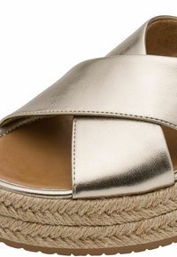 Metallisk guldsandale med krydsrem og en tekstureret overdel samt en naturlig jutesål med plateau. Blød indersål i lysebrun farve.