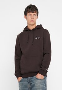 Mørkebrun hoodie lavet af blødt stof med en frontlomme, snoretrækshætte og hvidt broderet logo på venstre bryst.