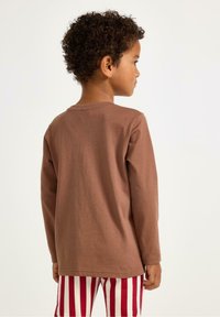 Ruskea pitkähihainen paita, joka on valmistettu pehmeästä kankaasta, yksinkertaisella pyöreällä pääntiellä, yhdistetty punavalkoraidallisiin housuihin.