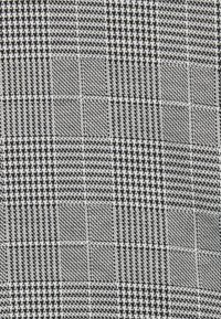 Tela de patrón houndstooth en blanco y negro con un tejido texturizado que presenta secciones alternas de cuadros pequeños y grandes.