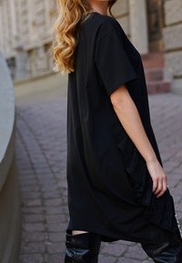 Czarna sukienka T-shirt o luźnym kroju, z plisowanym frędzlem po jednej stronie i krótkimi rękawami, zestawiona z czarnymi botkami do kolan.