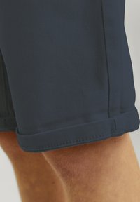 Shorts bleu marine en tissu texturé avec un ourlet replié. Présente des coutures visibles et une coupe ajustée autour de la cuisse.