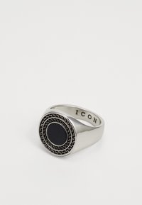 Anillo de plata con un centro de piedra negra circular rodeada de un patrón decorativo. Interior de la banda grabado con "ICON."